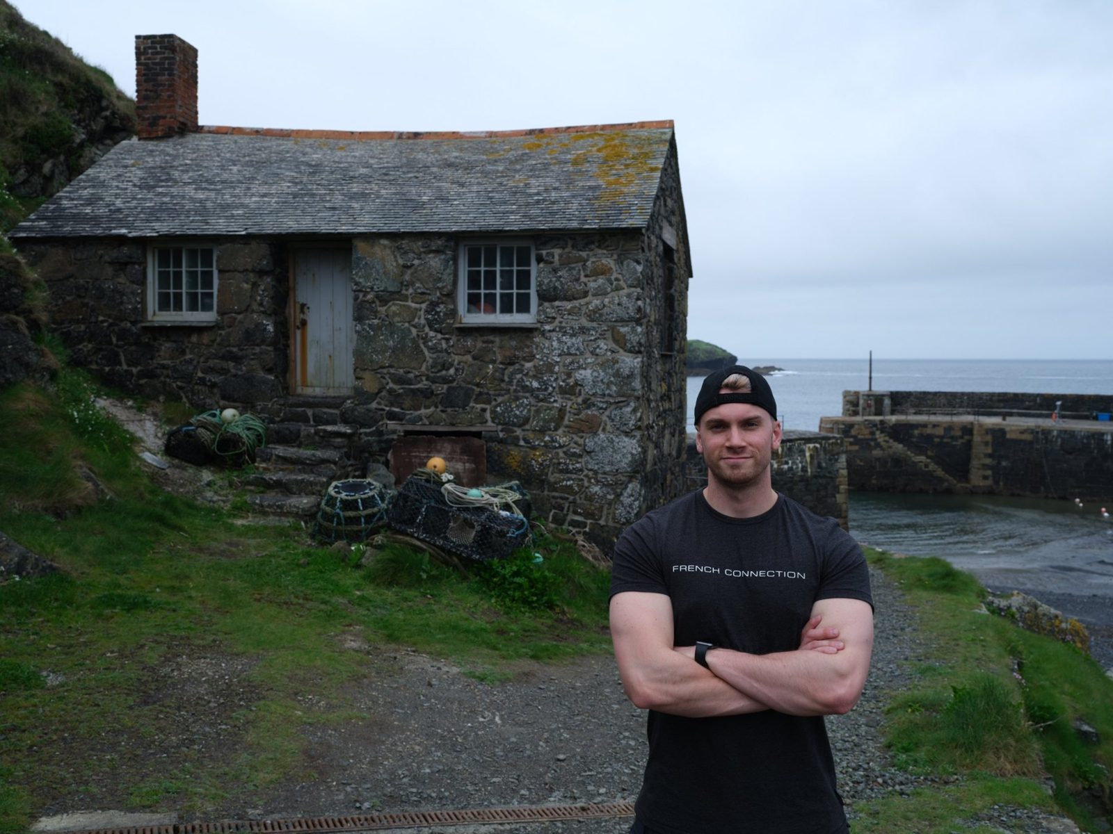 Terry standing beside a stone fisherman's cottage at a coastal harbor