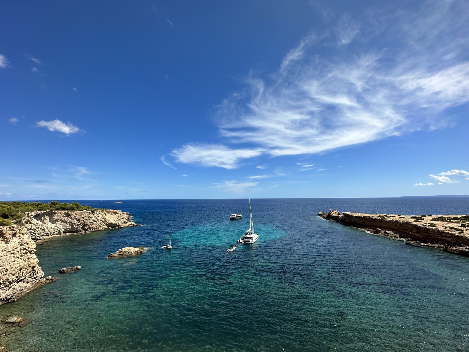 Turquoise cove with a private catamaran at anchor between rocky headlands